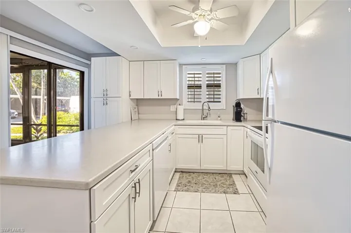 Kitchen featuring white appliances, a raised ceiling, white cabinets, light countertops, and a peninsula