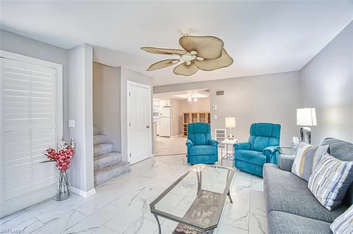 Living room with stairway, light marble finish floors, ceiling fan, and a chandelier