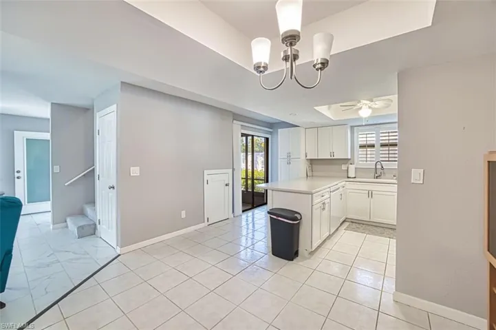 Kitchen with a raised ceiling, light countertops, white cabinets, a peninsula, and a chandelier