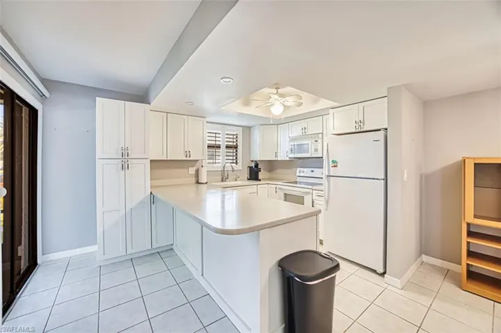 Kitchen with light countertops, white appliances, light tile patterned floors, white cabinets, and a peninsula