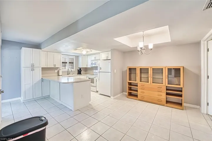 Kitchen with light countertops, white appliances, light tile patterned floors, white cabinetry, and a peninsula