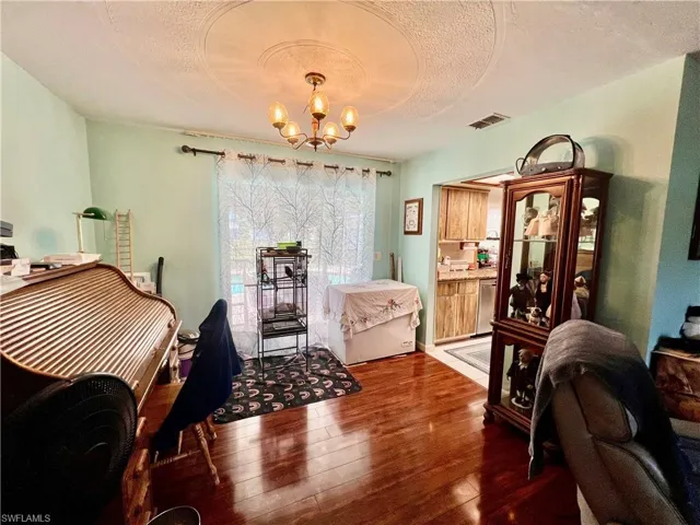 Dining room with dark wood-style flooring, visible vents, a textured ceiling, and an inviting chandelier