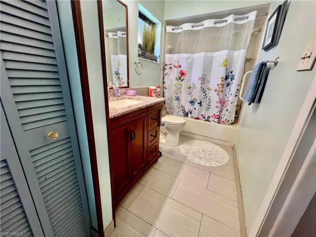 Bathroom featuring shower / tub combo, toilet, tile patterned flooring, vanity, and a linen closet