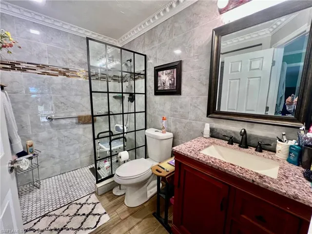Primary bathroom with a newly tiled walk in shower, toilet, tile floors, vanity, and tile walls