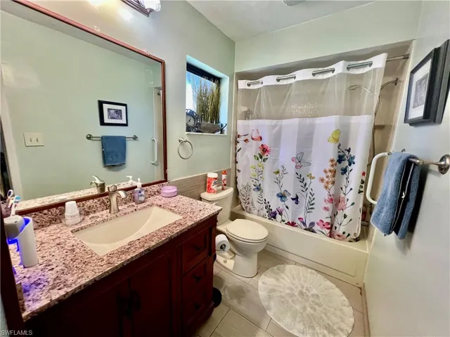Bathroom featuring toilet, tile patterned floors, vanity, and shower / bathtub combination with curtain