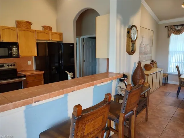 Kitchen featuring ornamental molding, tile countertops, light tile patterned floors, and black appliances