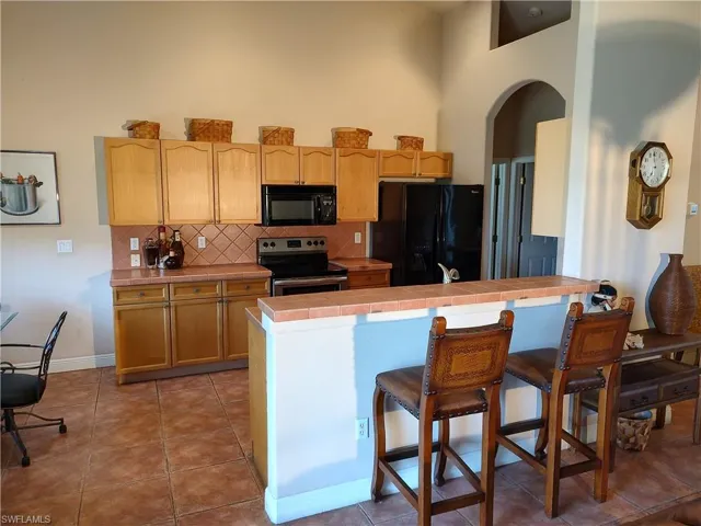 Kitchen with tasteful backsplash, tile countertops, tile patterned floors, and black appliances