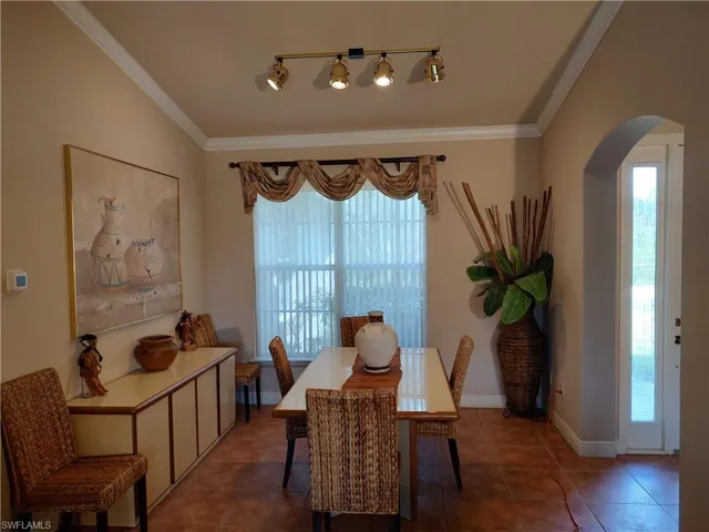 Dining area featuring arched walkways, dark tile patterned flooring, crown molding, and baseboards