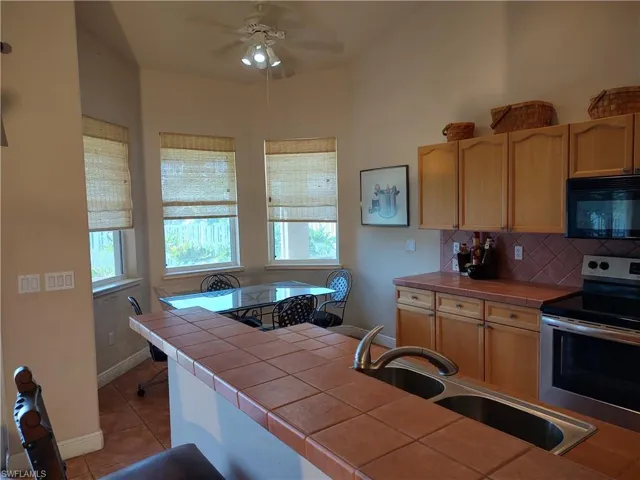Kitchen featuring sink, tile countertops, light tile patterned floors, electric stove, and decorative backsplash