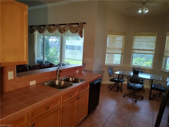 Kitchen featuring sink, crown molding, tile patterned flooring, black dishwasher, and tile countertops