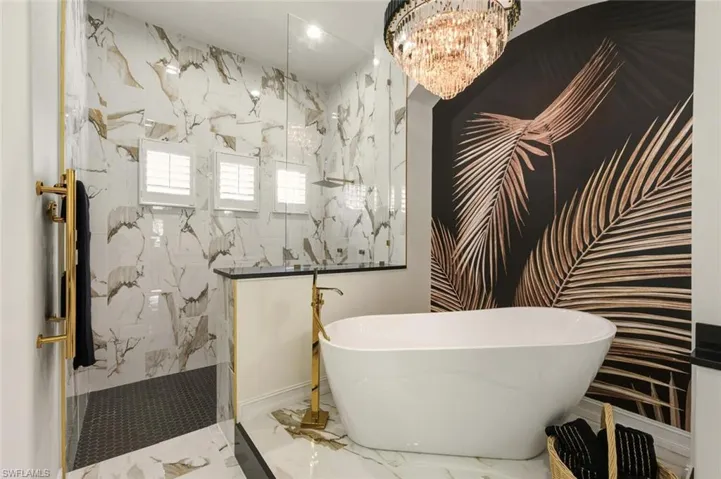 Full bath featuring a freestanding tub, a marble finish shower, a chandelier, marble tiled flooring, and stone wall
