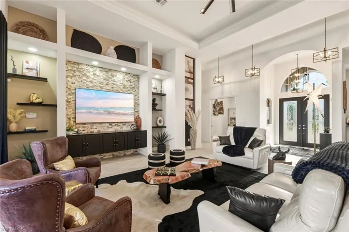 Tiled living area featuring built in shelves, a chandelier, ornamental molding, arched walkways, and a towering ceiling