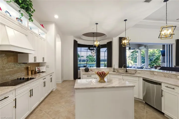 Kitchen with white cabinets, hanging light fixtures, backsplash, and light stone counters