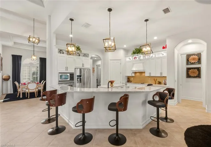 Kitchen featuring arched walkways, a breakfast bar, light stone counters, hanging light fixtures, and white cabinetry
