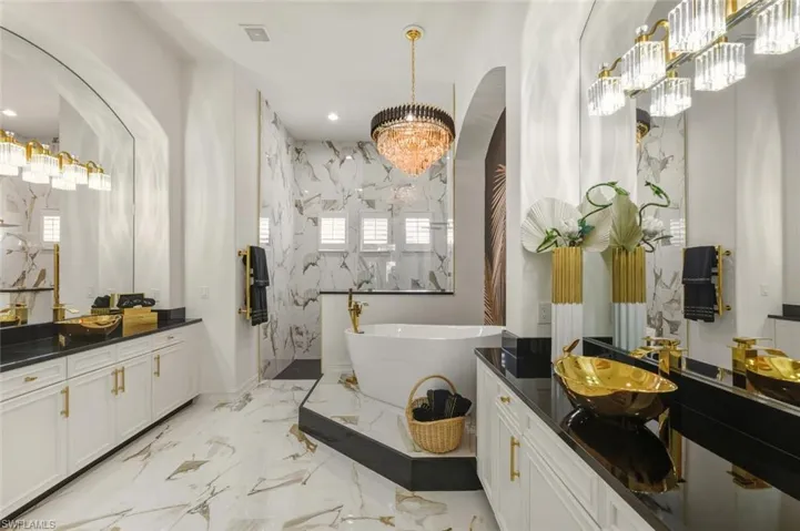 Bathroom with a soaking tub, two vanities, a marble finish shower, light marble finish flooring, and a chandelier