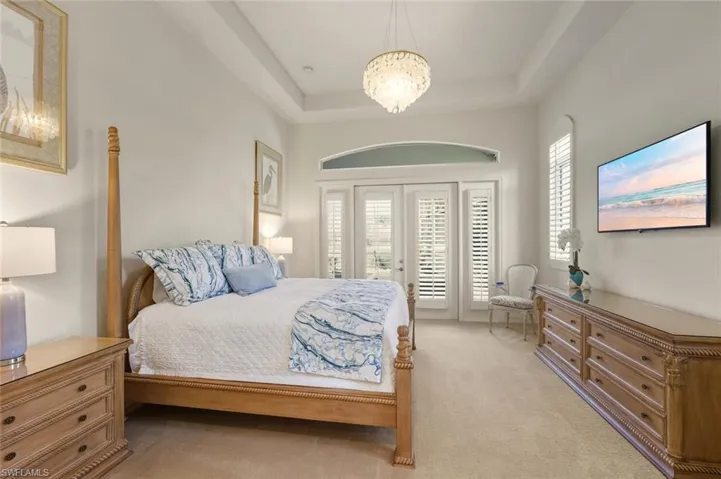 Carpeted bedroom with access to exterior, a chandelier, and a tray ceiling