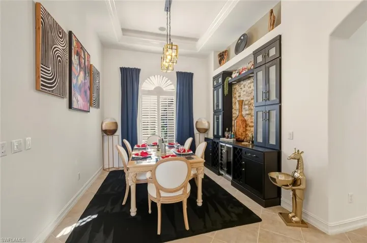 Dining room featuring light tile patterned floors, a chandelier, a raised ceiling, and beverage cooler