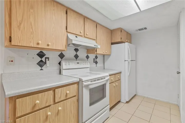 Kitchen with white appliances, backsplash, and light countertops