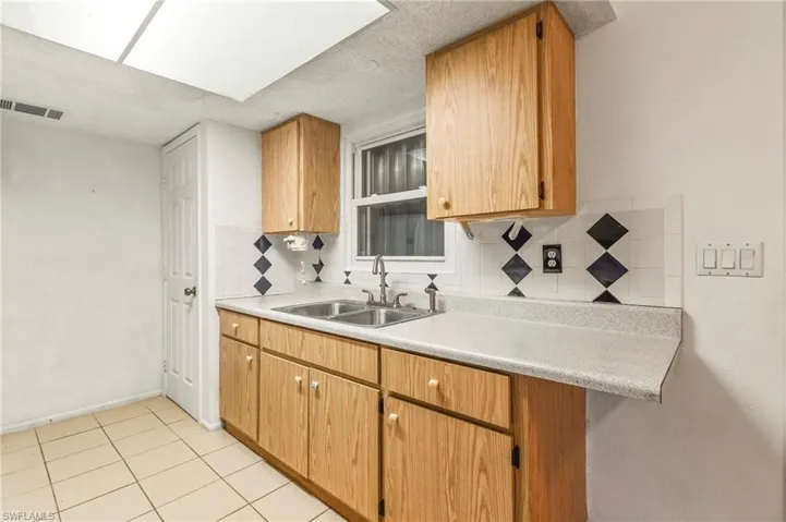Kitchen featuring light countertops, decorative backsplash, light tile patterned floors, wood finish cabinets, and a textured ceiling