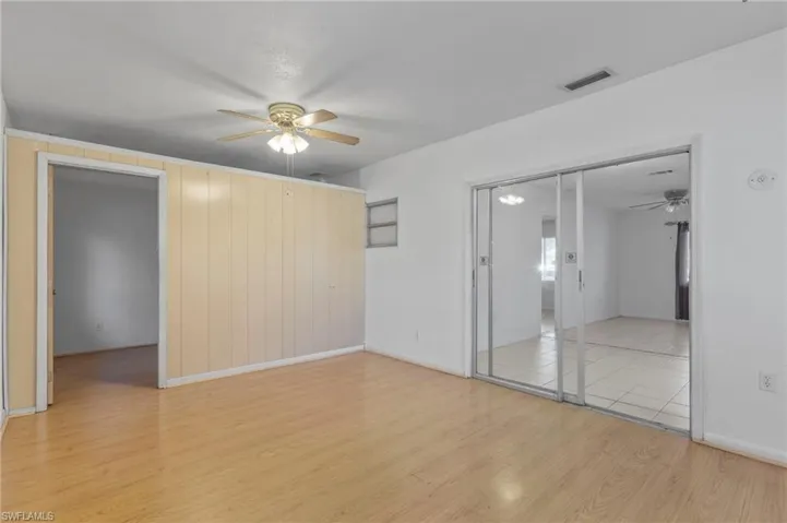 Unfurnished bedroom with light wood-style flooring, ceiling fan, a closet, and wood walls