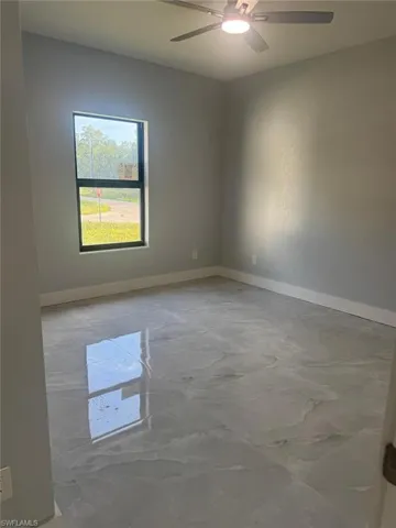 Unfurnished room with healthy amount of natural light, light marble finish flooring, and a ceiling fan
