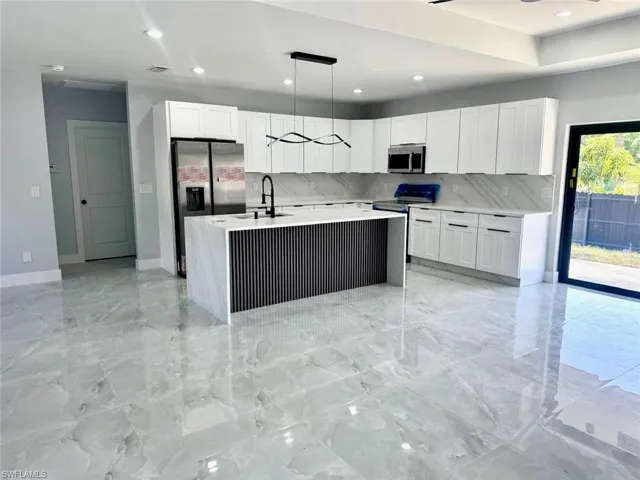 Kitchen featuring an island with sink, white cabinetry, light stone countertops, and recessed lighting
