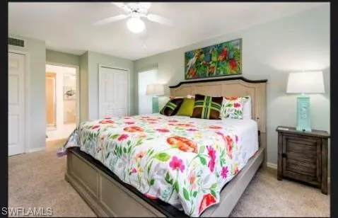 Bedroom with light colored carpet, ensuite bathroom, multiple closets, and ceiling fan