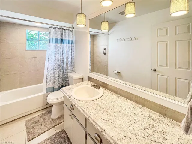 Full bathroom with tile patterned floors, shower / bathtub combination with curtain, toilet, and vanity