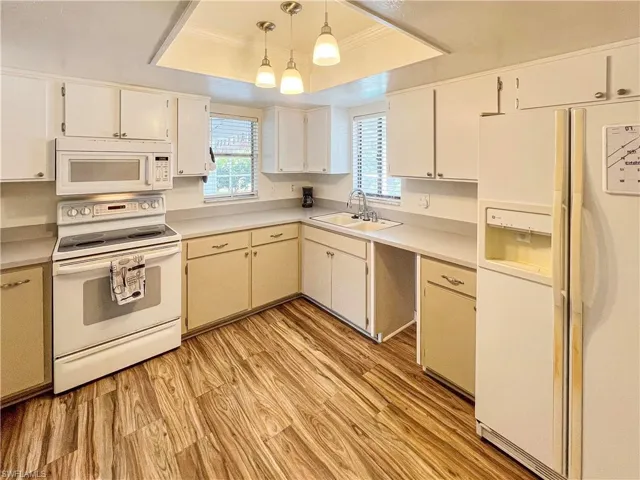 Kitchen with light hardwood / wood-style flooring, white appliances, pendant lighting, a raised ceiling, and sink
