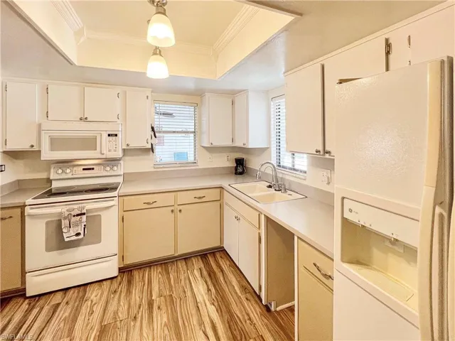 Kitchen featuring a wealth of natural light, light wood-type flooring, a raised ceiling, and white appliances