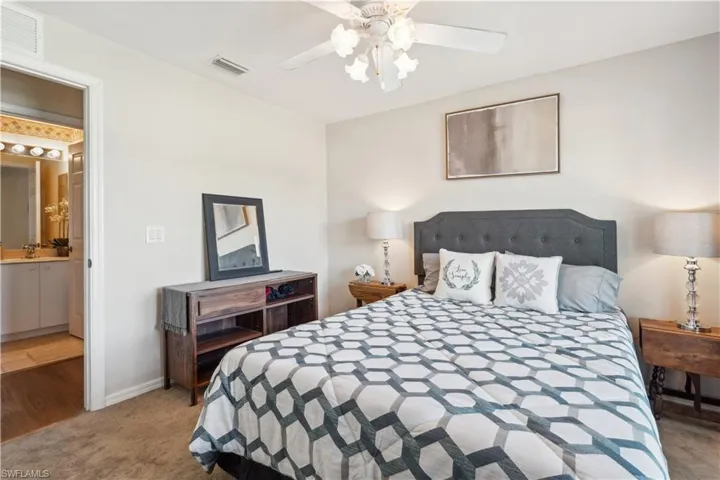 Carpeted bedroom with ceiling fan, ensuite bathroom, and sink