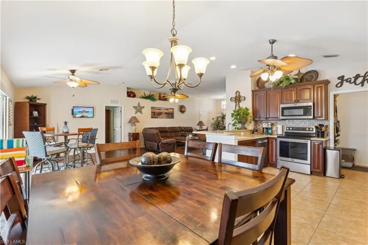 Tiled dining area featuring ceiling fan with notable chandelier and vaulted ceiling