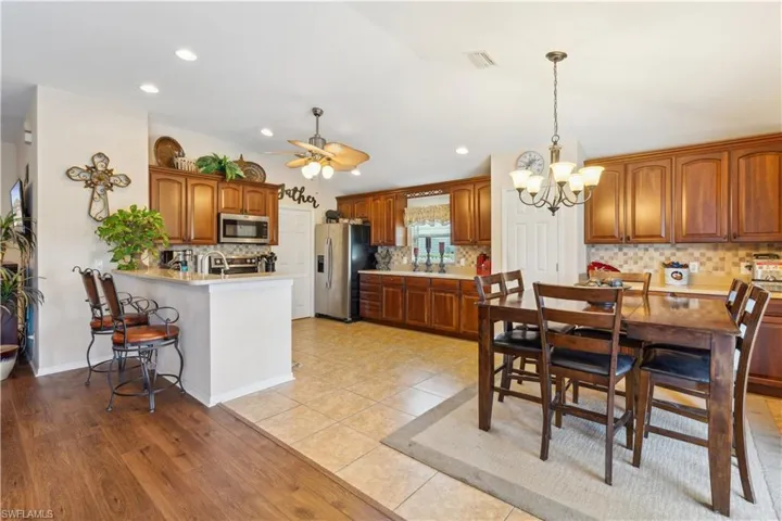 Kitchen with appliances with stainless steel finishes, hanging light fixtures, ceiling fan with notable chandelier, kitchen peninsula, and light wood-type flooring