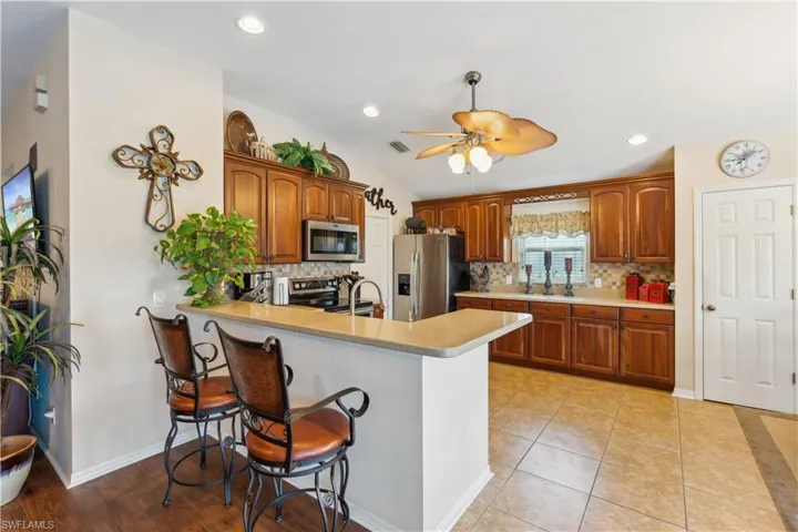 Kitchen with ceiling fan, kitchen peninsula, a kitchen bar, appliances with stainless steel finishes, and vaulted ceiling