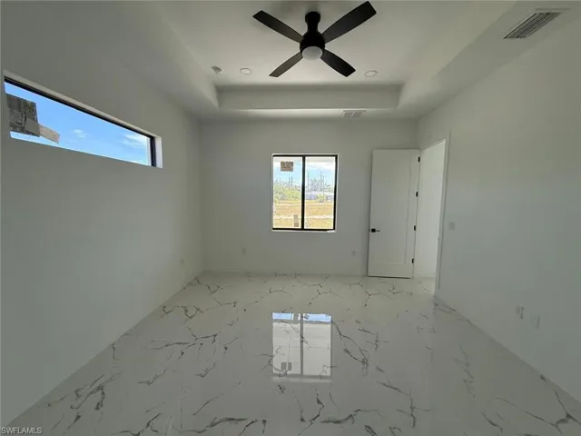 Empty room featuring a raised ceiling, a healthy amount of sunlight, and ceiling fan