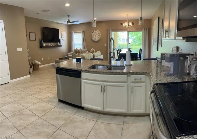 Kitchen with stone counters, stainless steel appliances, sink, ceiling fan with notable chandelier, and white cabinetry