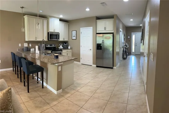 Kitchen with light tile patterned floors, kitchen peninsula, appliances with stainless steel finishes, a kitchen breakfast bar, and sink