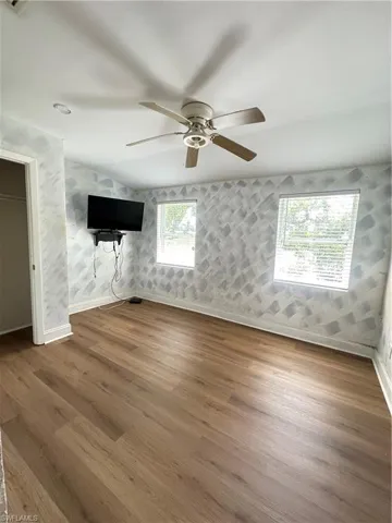 Unfurnished living room with wallpapered walls, wood finished floors, and ceiling fan