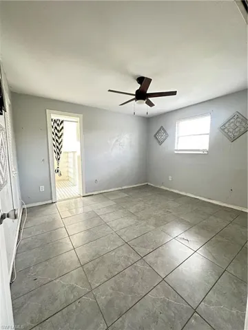 Tiled empty room with a ceiling fan and baseboards