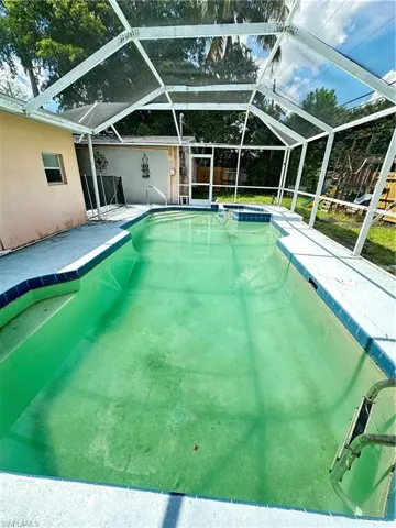 View of swimming pool featuring a patio area, a sunroom, a pool with connected hot tub, and glass enclosure