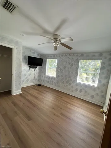 Unfurnished bedroom featuring wallpapered walls, wood finished floors, and a ceiling fan