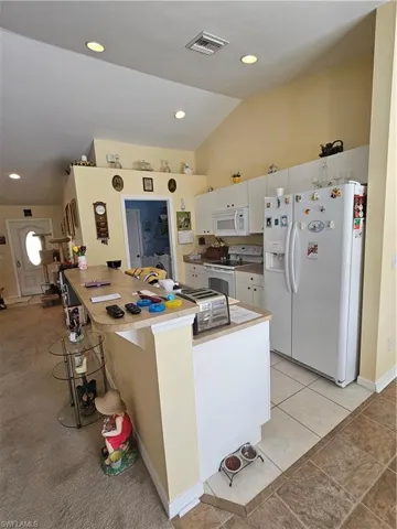 Kitchen with light tile patterned floors, appliances with stainless steel finishes, white cabinetry, high vaulted ceiling, and a breakfast bar