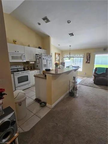 Kitchen with refrigerator, stove, a center island, lofted ceiling, and white cabinets