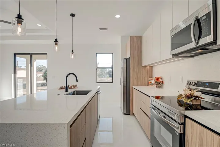 Kitchen featuring modern cabinets, stainless steel appliances, recessed lighting, and light stone counters
