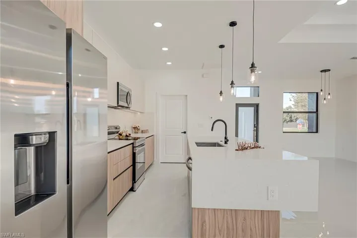 Kitchen with appliances with stainless steel finishes, modern cabinets, hanging light fixtures, recessed lighting, and light stone counters