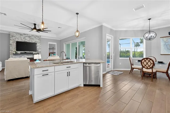 Kitchen featuring wood finish floors, crown molding, hanging light fixtures, white cabinets, and a raised ceiling