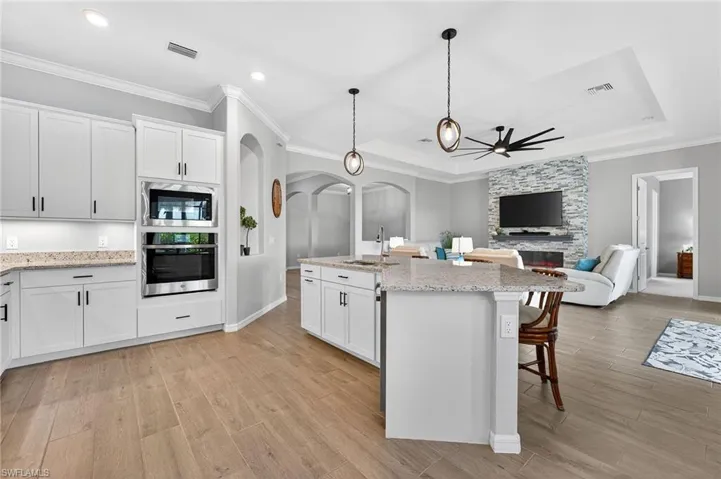 Kitchen with white cabinetry, ceiling fan, arched walkways, pendant lighting, and ornamental molding