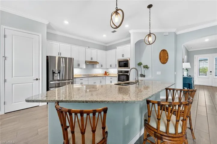 Kitchen featuring crown molding, appliances with stainless steel finishes, a kitchen bar, light stone countertops, and white cabinets