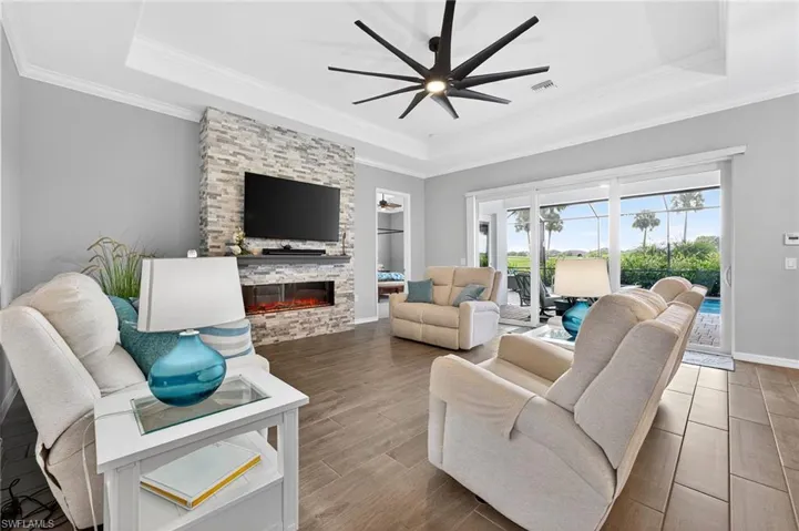 Living room with a tray ceiling, wood finished floors, a ceiling fan, crown molding, and a stone fireplace