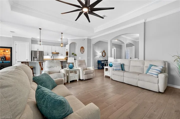 Living room with crown molding, arched walkways, light wood finished floors, and ceiling fan